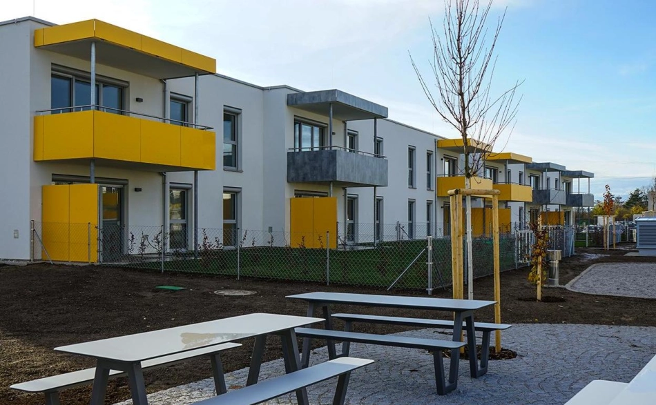 EBSG Außenansicht einer Wohnanlage mit gelben Balkonen, Sitzgelegenheiten und neu gepflanzten Bäumen, Lachtengasse.